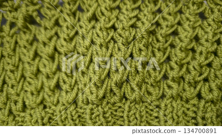 Knitting pattern using thick green yarn. Needles, thread, and green fabric 134700891