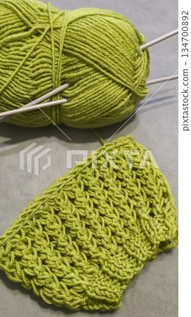 Knitting pattern using thick green yarn. Needles, thread, and green fabric 134700892