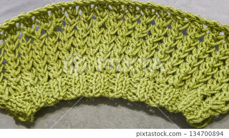 Knitting pattern using thick green yarn. Needles, thread, and green fabric 134700894