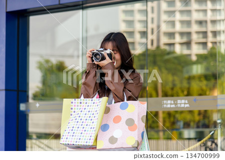 Asian woman shopping, people enjoying lifestyle, holding fashion bags, capturing moments with camera near modern mall, depicting retail excitement and vibrant city life Asian woman shopping, people enjoying lifestyle, holding fashion bags, capturing moments with camera near modern mall, depicting retail excitement and vibrant city life 134700999
