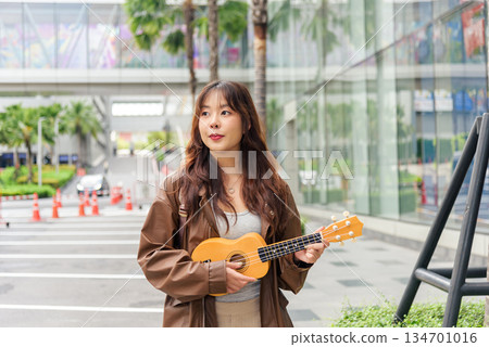 Young woman happy person travel tourist enjoys holiday music, playing ukulele outdoors on vibrant urban city street, embracing summer lifestyle with joyful expression, walking among modern buildings Young woman happy person travel tourist enjoys holiday music, playing ukulele outdoors on vibrant urban city street, embracing summer lifestyle with joyful expression, walking among modern buildings 134701016