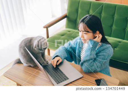 一隻貓和一位女士一起看著電腦。 134701449