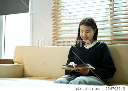 Young woman reading a book on the sofa, enjoying a calm and relaxing moment at home Young woman reading a book on the sofa, enjoying a calm and relaxing moment at home 134703343