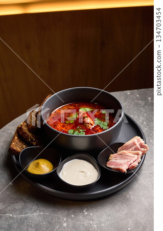 Traditional Ukrainian borscht soup with sourdough bread mustard sour cream and bacon on rustic table culinary presentation concept 134703454