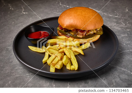 Gourmet burger with fries, ketchup, black plate, appetizing food presentation, delicious meal concept 134703465