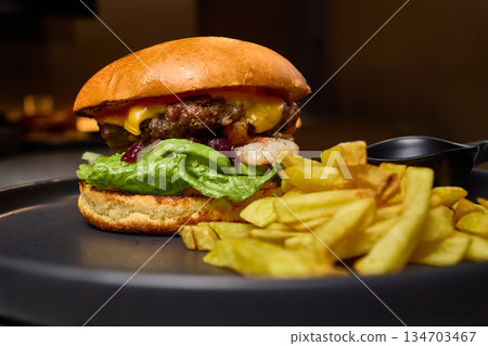 Juicy beef burger with melted cheese, fresh lettuce and crispy fries on a plate ready to eat delicious food concept 134703467