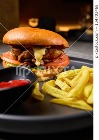 Gourmet Cheeseburger with Juicy Chicken, Fresh Vegetables, Crispy Fries, and Ketchup on Black Plate, Delicious Fast Food Meal Concept Gourmet Cheeseburger with Juicy Chicken, Fresh Vegetables, Crispy Fries, and Ketchup on Black Plate, Delicious Fast Food Meal Concept 134703469