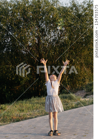 Happy girl walking in a summer field. A girl with a white flower in her hands. A joyful girl. Happy girl walking in a summer field. A girl with a white flower in her hands. A joyful girl. 134703575