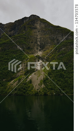 Mountain and river. Clear water flowing at base of rocky peak, green landscape, calm atmosphere.  134703578