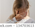 The girl covers her eyes with her hands. The child experiences embarrassment or fear. 134703613