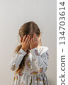 The girl covers her eyes with her hands. The child experiences embarrassment or fear. 134703614