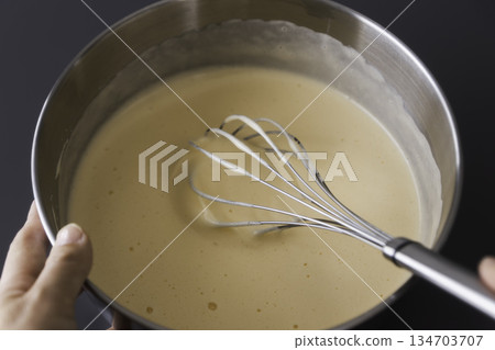 Hands mixing cake batter with a whisk and a bowl 134703707