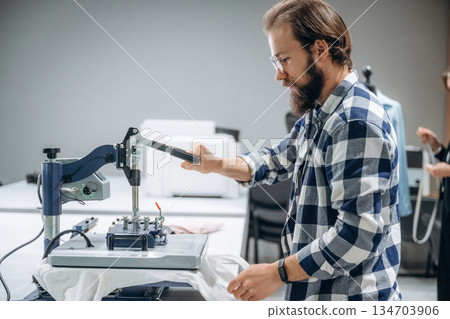 Guy in checkered shirt is working. People are by the sewing machines indoors Guy in checkered shirt is working. People are by the sewing machines indoors 134703906