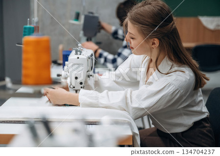 View from the side, sitting. People are working by the sewing machines indoors View from the side, sitting. People are working by the sewing machines indoors 134704237