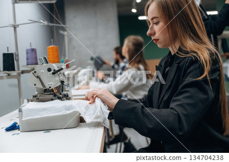 Job of clothing production. People are working by the sewing machines indoors Job of clothing production. People are working by the sewing machines indoors 134704238