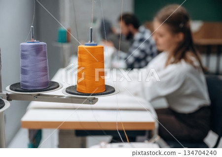 View from the side, sitting. People are working by the sewing machines indoors View from the side, sitting. People are working by the sewing machines indoors 134704240