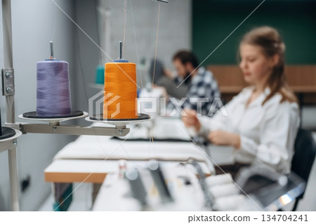 View from the side, sitting. People are working by the sewing machines indoors View from the side, sitting. People are working by the sewing machines indoors 134704241