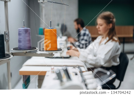 View from the side, sitting. People are working by the sewing machines indoors View from the side, sitting. People are working by the sewing machines indoors 134704242