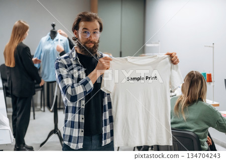 T-shirt with sample print text on it. People are working by the sewing machines indoors T-shirt with sample print text on it. People are working by the sewing machines indoors 134704243