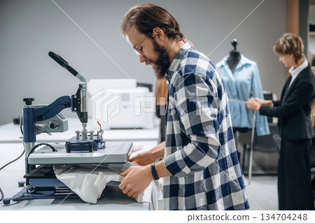 Guy in checkered shirt is working. People are by the sewing machines indoors 134704248
