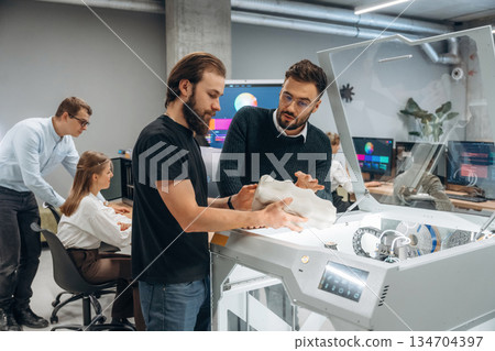 Communication, finished printed object. People are in the office by the 3d printer 134704397