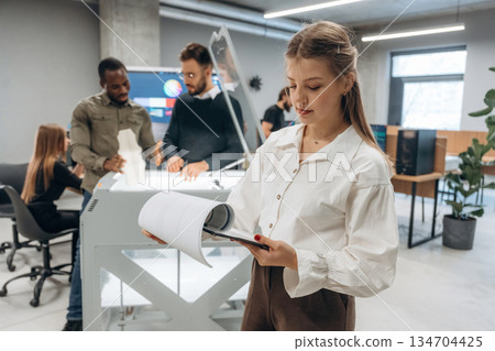 Holding notepad, woman is standing. People are in the office by the 3d printer Holding notepad, woman is standing. People are in the office by the 3d printer 134704425