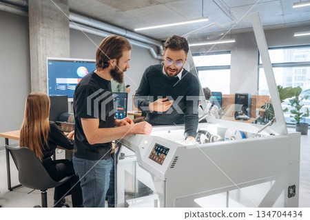 Showing the 3d printer. People are in the office 134704434