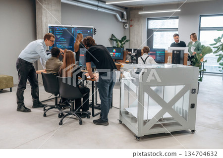 Big screen with code on the wall. People are in the office by the 3d printer 134704632
