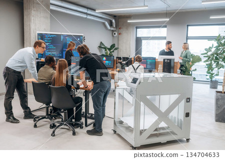 Big screen with code on the wall. People are in the office by the 3d printer Big screen with code on the wall. People are in the office by the 3d printer 134704633