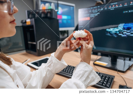 By computer, sitting. Woman is holding 3d printed toy turtle 134704717