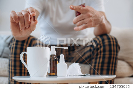 Table with cup and spray. Guy is sitting and taking a pills, feeling sick, bad 134705035