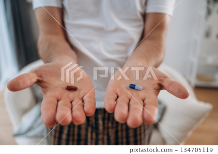 Man is sitting and holding red and blue pills in hands Man is sitting and holding red and blue pills in hands 134705119