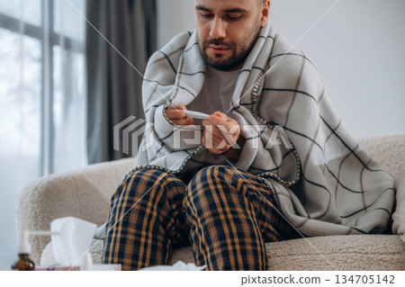 Checking body temperature with thermometer. Sick man is feeling bad at home 134705142