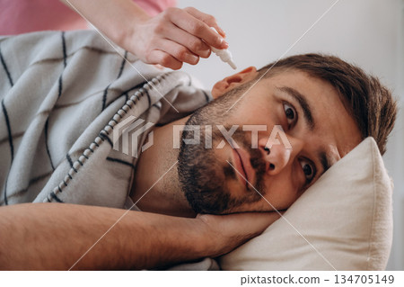 A man lies on a bed. A woman puts ear drops in his ear A man lies on a bed. A woman puts ear drops in his ear 134705149