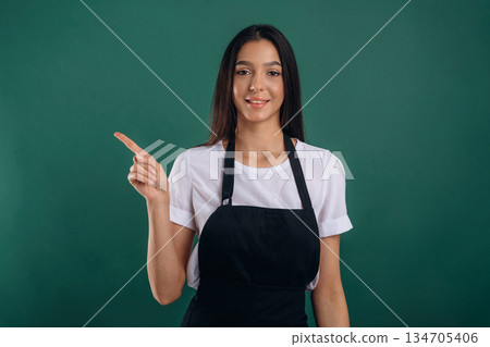 Pointing finger to a side. Young beautiful barista is against background 134705406