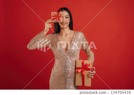 Front view, new year, with presents. Young elegant woman is against background Front view, new year, with presents. Young elegant woman is against background 134705439