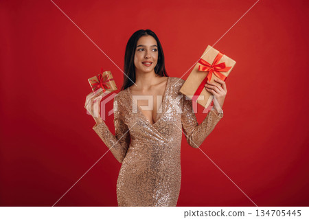 Positive facial expression, gifts in hands. Young elegant woman is against background 134705445