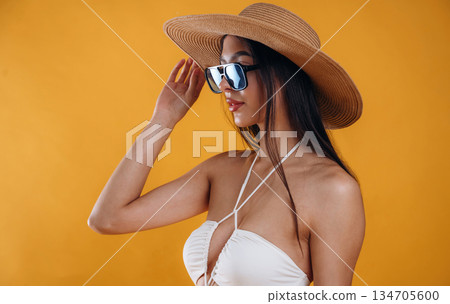 Side view, standing, in sunglasses and straw hat. Young beautiful tourist woman is against background Side view, standing, in sunglasses and straw hat. Young beautiful tourist woman is against background 134705600