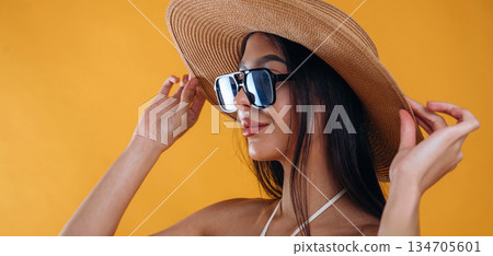 Side view, standing, in sunglasses and straw hat. Young beautiful tourist woman is against background Side view, standing, in sunglasses and straw hat. Young beautiful tourist woman is against background 134705601