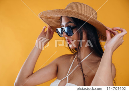 Side view, standing, in sunglasses and straw hat. Young beautiful tourist woman is against background Side view, standing, in sunglasses and straw hat. Young beautiful tourist woman is against background 134705602