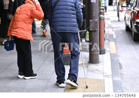 End of the year cityscape in Tokyo, Japan. Aging society. An elderly woman can't hail a taxi and calls one by cell phone. A man with a cane has difficulty walking... 134705648