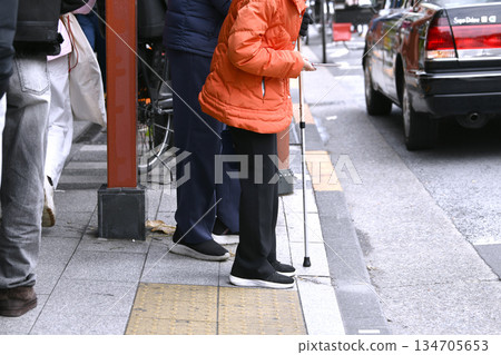 End of the year cityscape in Tokyo, Japan. Aging society. An elderly woman can't hail a taxi and calls one by cell phone. A man with a cane has difficulty walking... 134705653