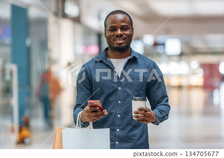 Cup of drink and shopping bags. Black man is in the hall of the supermarket 134705677