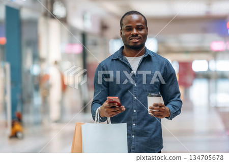 Cup of drink and shopping bags. Black man is in the hall of the supermarket 134705678