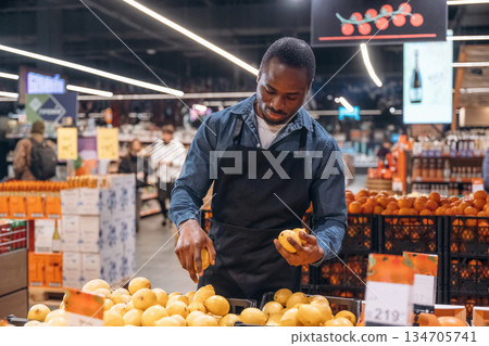 Fresh fruits. Grocery store worker in apron is near products 134705741