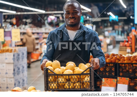 Fresh fruits. Grocery store worker in apron is near products 134705744