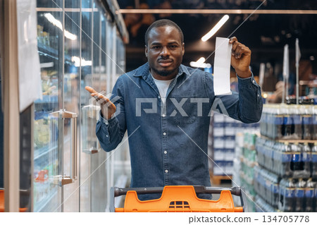 Disappointed with cost, holding check. Man customer is in the supermarket Disappointed with cost, holding check. Man customer is in the supermarket 134705778