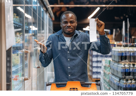 Disappointed with cost, holding check. Man customer is in the supermarket Disappointed with cost, holding check. Man customer is in the supermarket 134705779