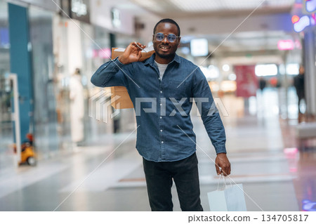 Walking and holding shopping bags. Black man is in the hall of the supermarket Walking and holding shopping bags. Black man is in the hall of the supermarket 134705817