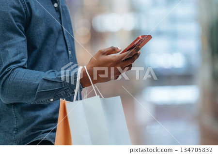Scrolling internet in smartphone. Close up view of man with shopping bags that is in the supermarket Scrolling internet in smartphone. Close up view of man with shopping bags that is in the supermarket 134705832